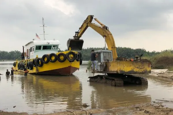 Yellow metal cargo work boat beached alongside an excavator at Port Klang